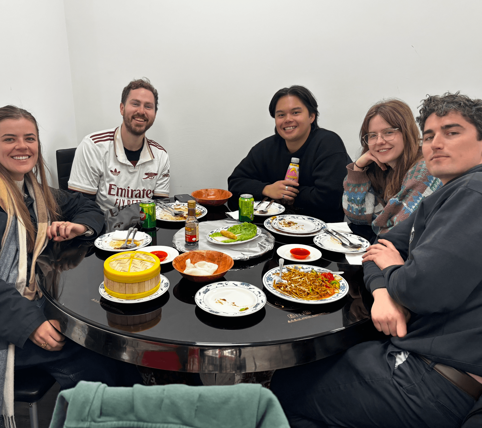 Friends smiling around a table of dim sum and noodles
